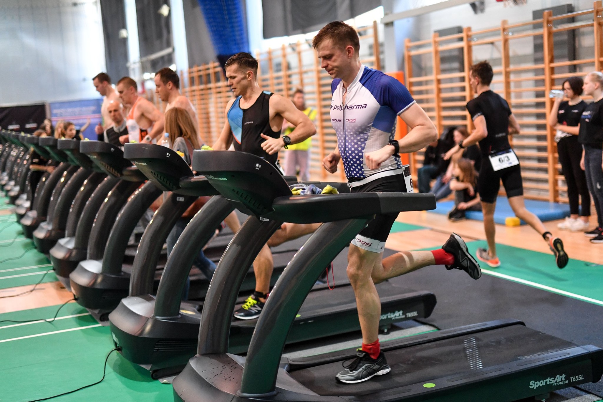 zawodnicy biegnący na bieżni rywalizujący ze sobą w hali w ramach indoor triathlonu