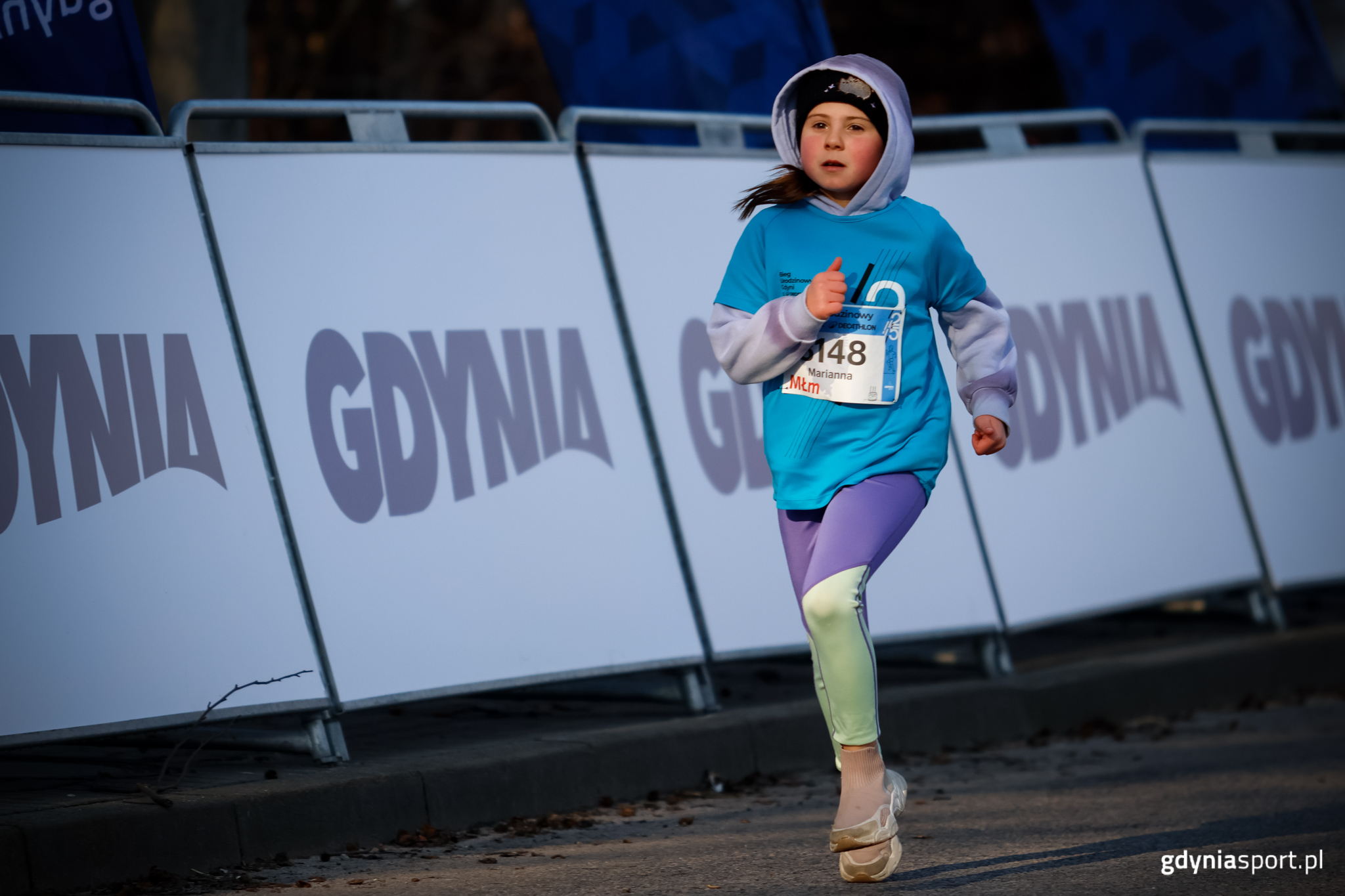 młoda zawodniczka podczas biegu w tle bandy z logiem miasta