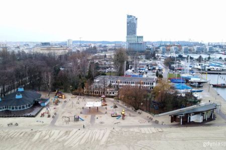 Zdjęcie plaży Gdynia Śródmieście z drona. na dole zdjęcia plaża i wymieniona kładki, na górnej części panorama Gdyni z Sea Towers