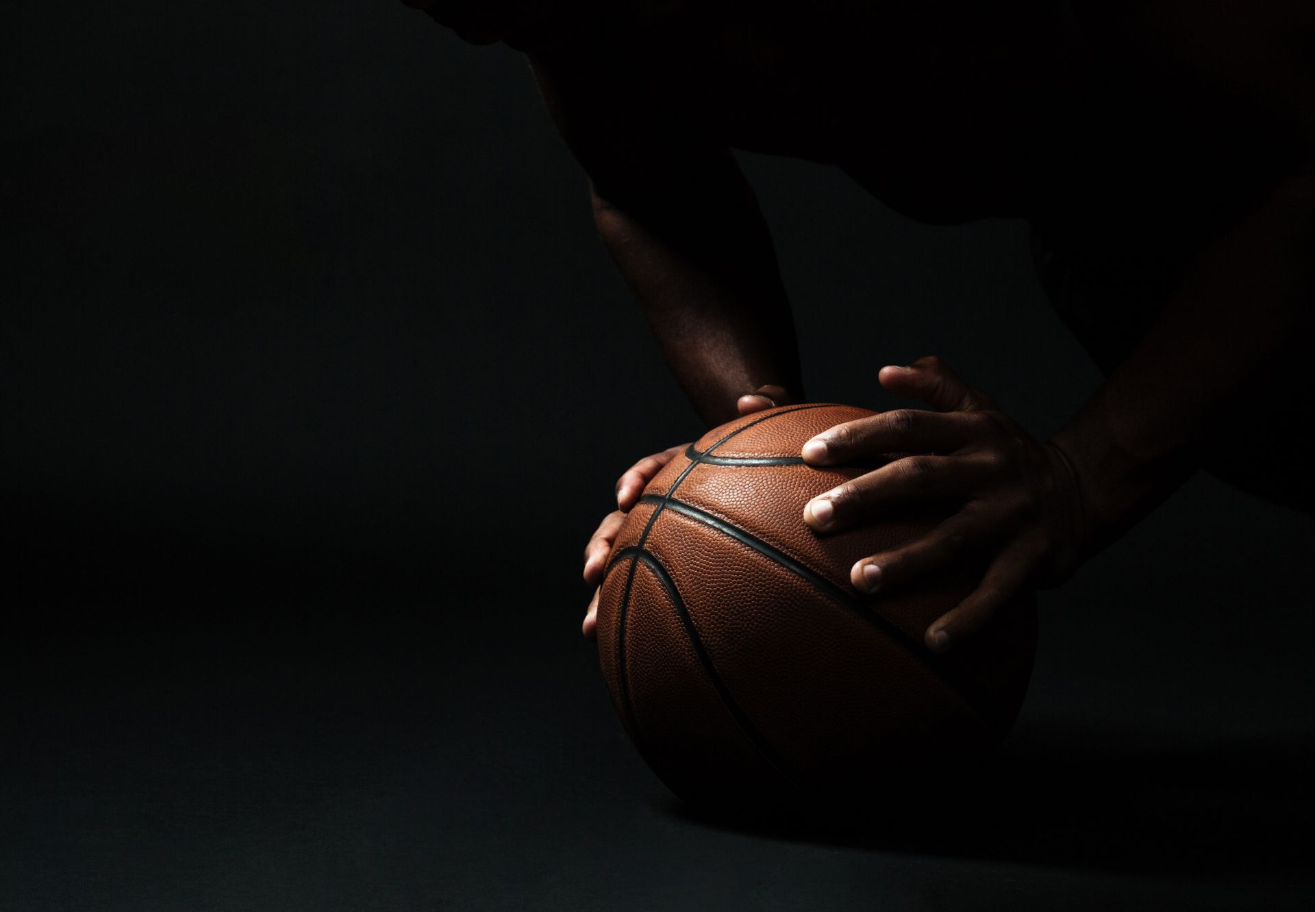 kosz do koszykówki w dłoniach zawodnika, który jest zaciemniony 