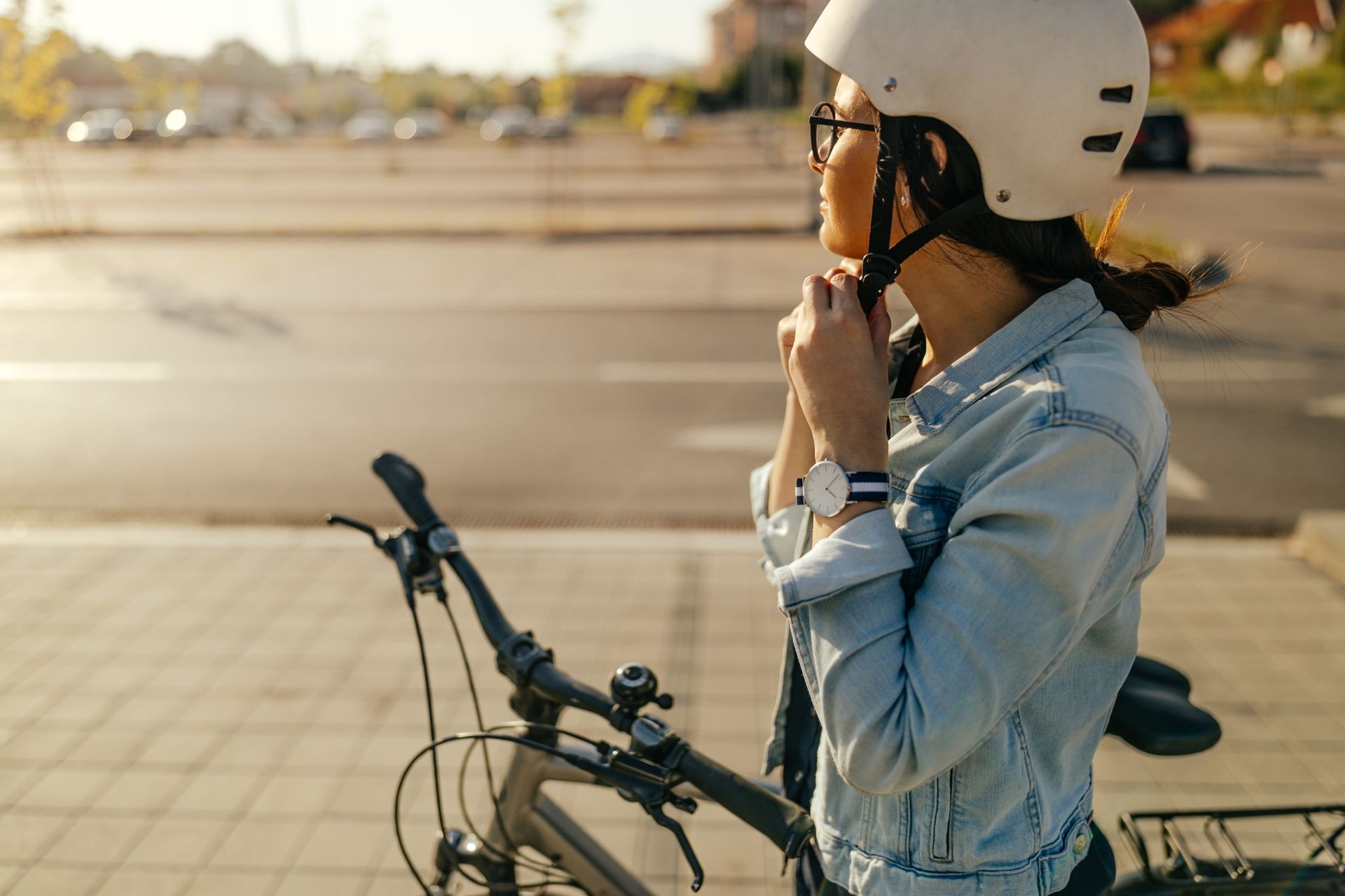 dziewczyna z rowerem zapinająca kask na tle ulicy 