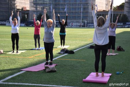 Osoby ćwiczące jogę na murawie stadionu