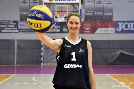 Alice Kunek w czarnej koszulce z napisem Gdynia trzymająca żółto-niebieska piłkę do koszykówki firmy Spalding