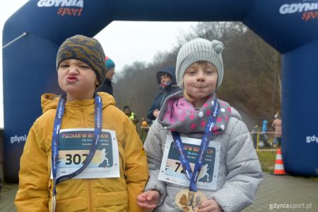 chłopiec i dziewczynka z medalami na tle bramy robiące śmieszne miny